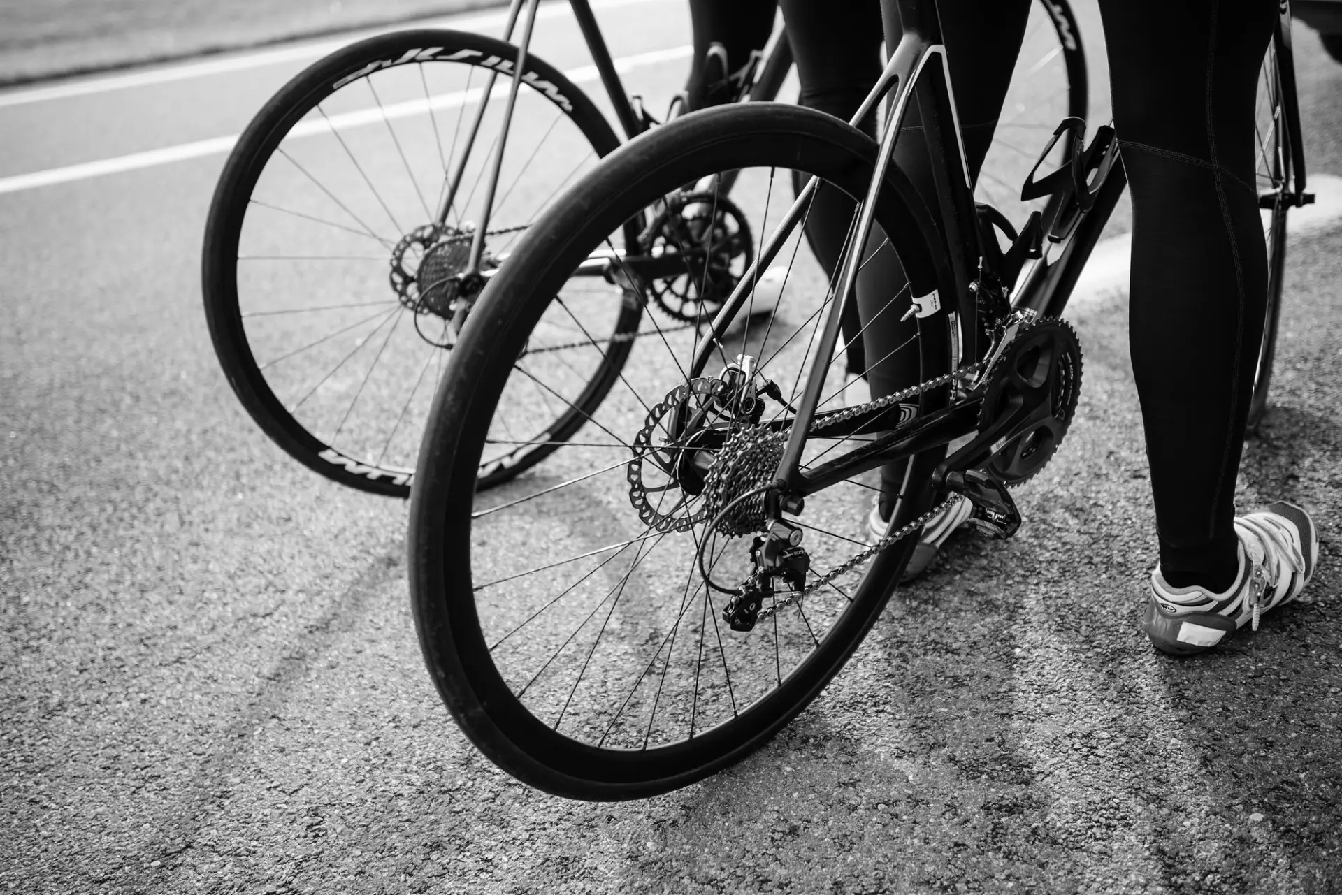 Schwarz-Weiß-Detail von Rennrad-Laufrädern und Scheibenbremse auf Asphalt