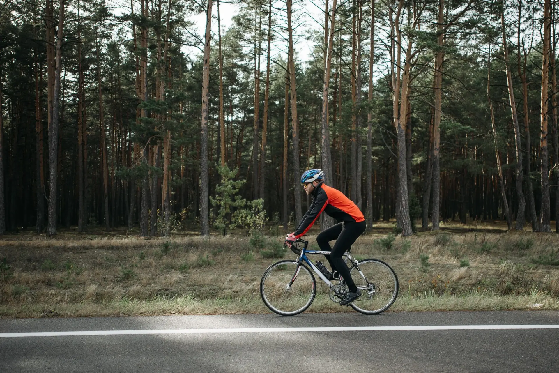 Rennradfahrer im orangefarbenen Trikot auf einer Landstraße am Waldrand